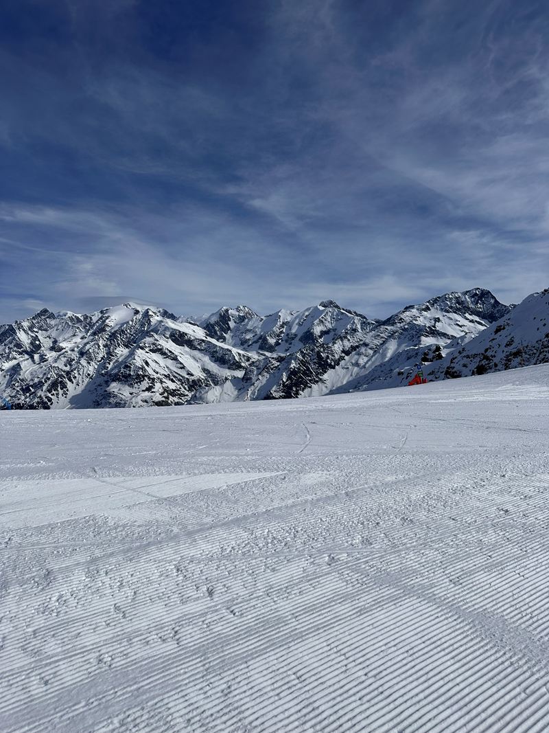 A freshly groomed ski run below snowy peaks