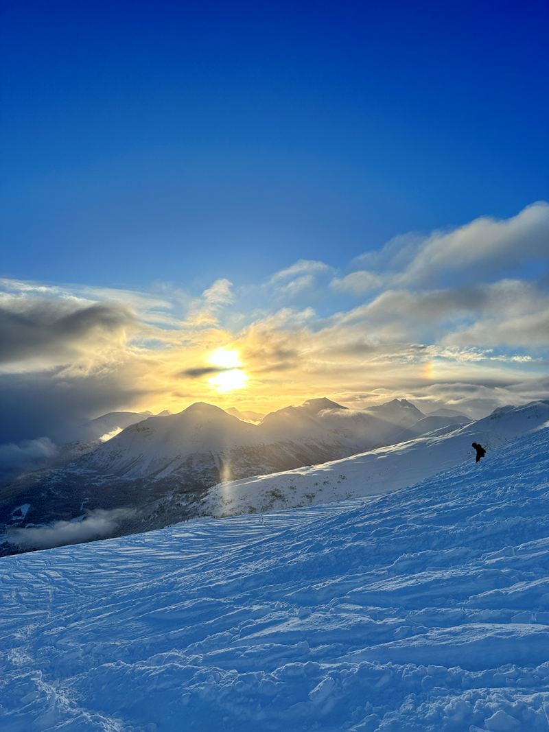 The sun setting over a ski slope and distant peaks