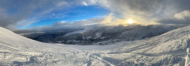 Panorama from a ski slope, with the sun breaking through clouds over the mountains
