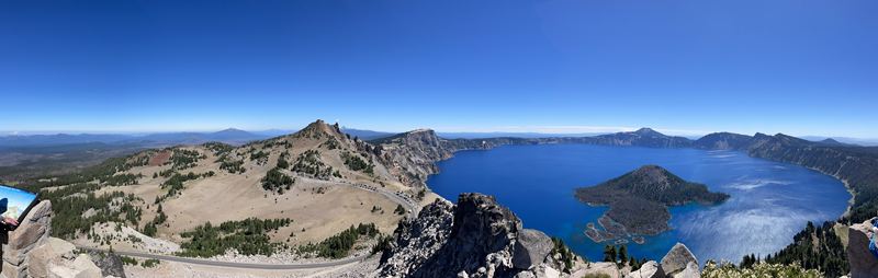 Panorama of a deep blue crater lake with a small island, seen from the rim