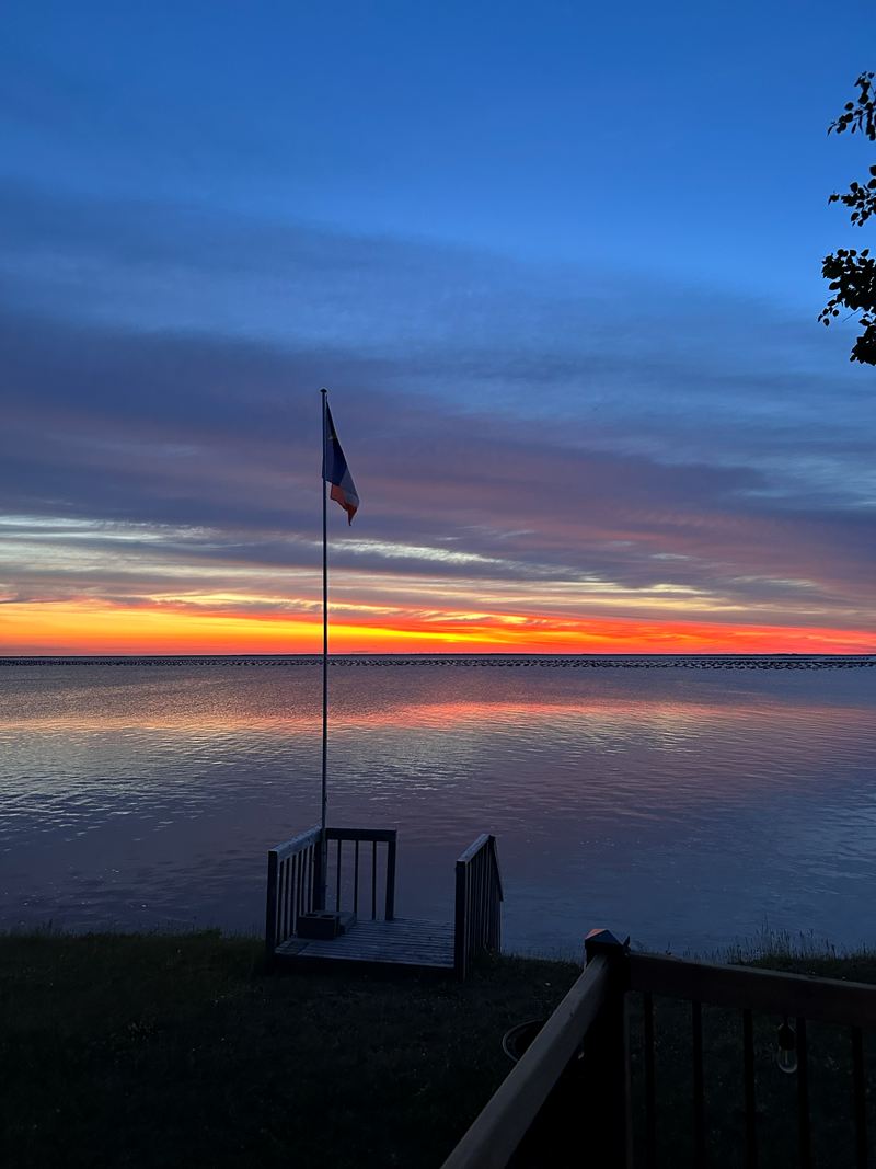 A flagpole silhouetted against a sunset over the water