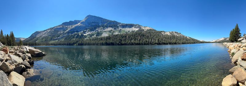 Panorama of a clear mountain lake with a granite peak behind it