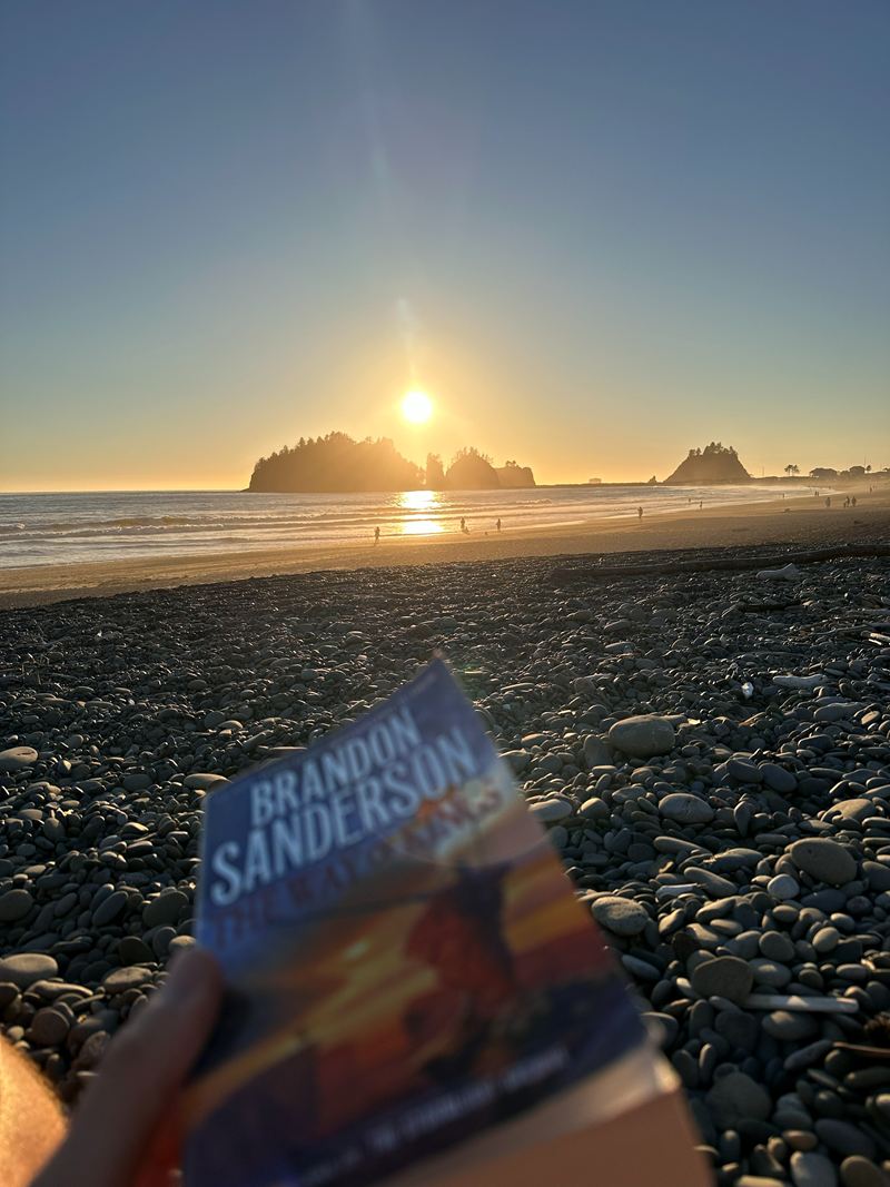 A book held up on a pebble beach at sunset